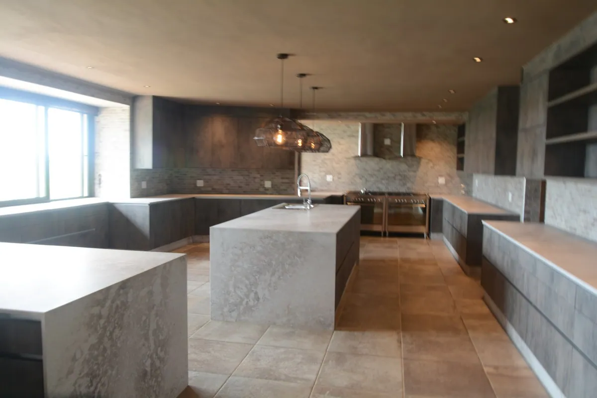 A large marble-topped island in an open-plan FKC kitchen, lit by copper pendant lights.